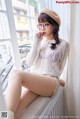 A woman sitting on a window sill wearing glasses and a beret.