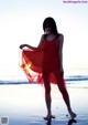 A woman in a red dress standing on the beach.