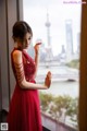 A woman in a red dress standing by a window.