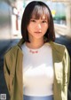 A woman in a white top and green jacket standing on a street.