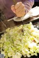 A person cutting up a pile of cabbage with a knife.