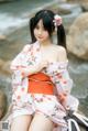 A woman in a pink kimono sitting on a rock by the water.