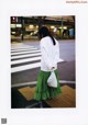 A woman in a white sweatshirt and green skirt crossing the street.