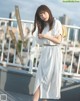 A woman in a white shirt dress and straw hat standing on a balcony.