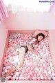 A woman laying in a bathtub filled with pink and white balloons.