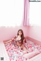 A woman sitting in a bathtub filled with pink and white balloons.