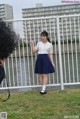 A woman in a white shirt and blue skirt standing next to a fence.